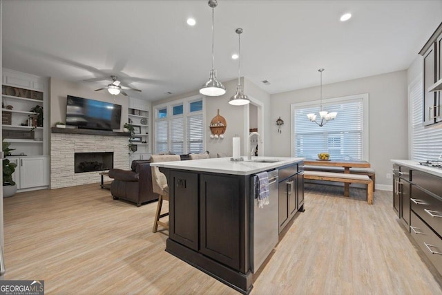 kitchen with sink, a center island with sink, dishwasher, pendant lighting, and a fireplace