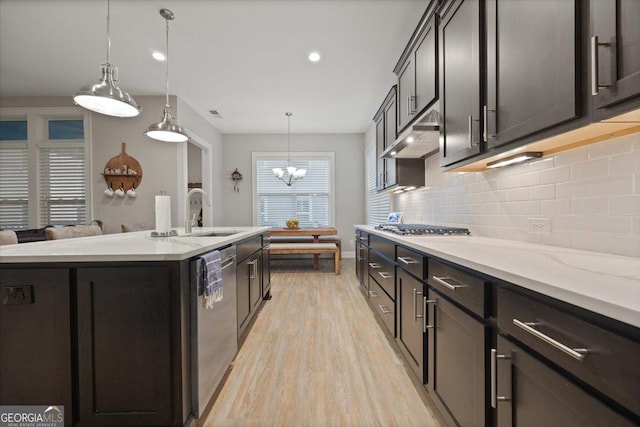 kitchen with sink, an island with sink, pendant lighting, stainless steel appliances, and backsplash