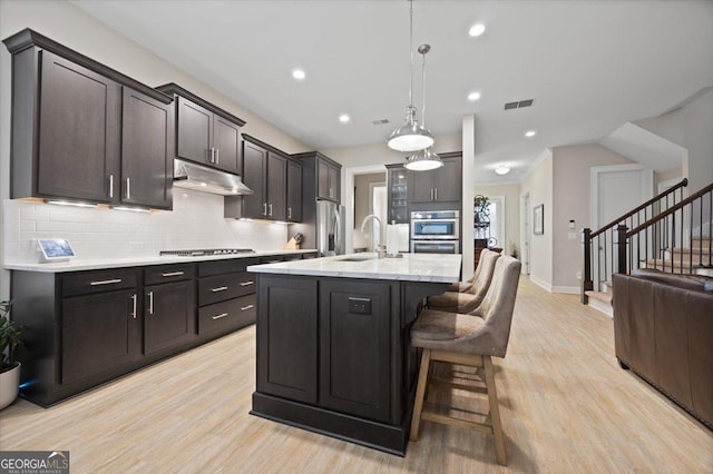 kitchen with appliances with stainless steel finishes, decorative light fixtures, tasteful backsplash, an island with sink, and sink