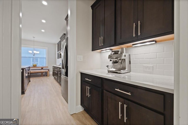 kitchen featuring hanging light fixtures, tasteful backsplash, light stone counters, and dark brown cabinetry