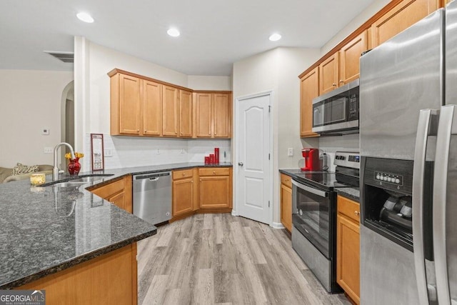 kitchen featuring sink, appliances with stainless steel finishes, light hardwood / wood-style floors, decorative backsplash, and dark stone counters