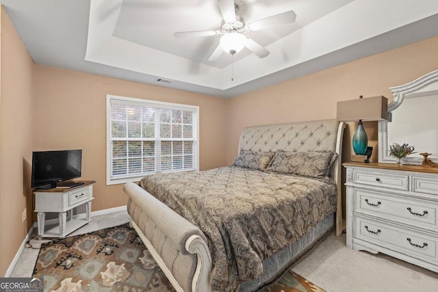 carpeted bedroom featuring ceiling fan and a tray ceiling