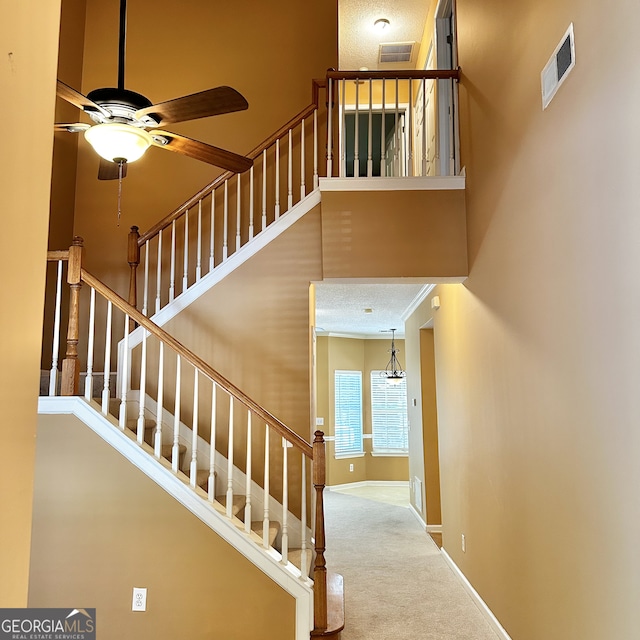 staircase with ceiling fan, a high ceiling, carpet, and a textured ceiling