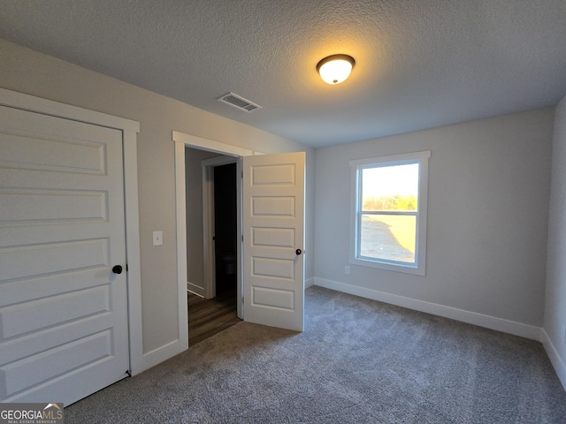 unfurnished room featuring a textured ceiling and dark colored carpet