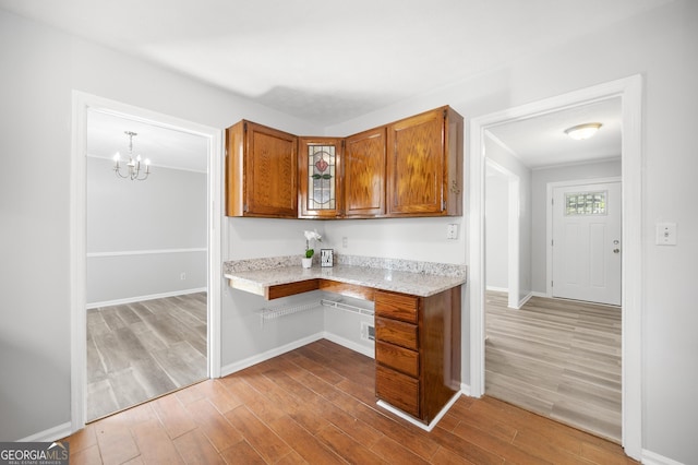 kitchen featuring light stone counters, built in desk, light hardwood / wood-style floors, and hanging light fixtures