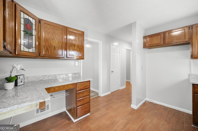 kitchen with light stone counters, built in desk, and light wood-type flooring