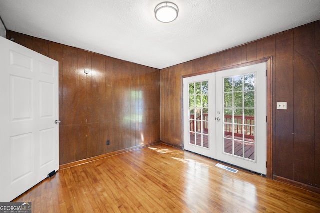 spare room with hardwood / wood-style floors, a textured ceiling, wooden walls, and french doors