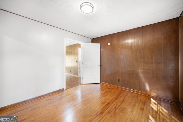 empty room with light hardwood / wood-style flooring, wooden walls, and a textured ceiling