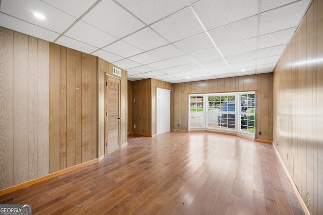 spare room with a paneled ceiling, wooden walls, and hardwood / wood-style floors