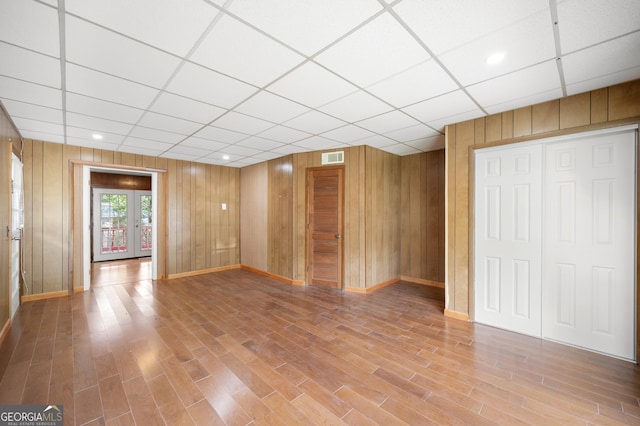 unfurnished living room with french doors, a paneled ceiling, hardwood / wood-style floors, and wood walls