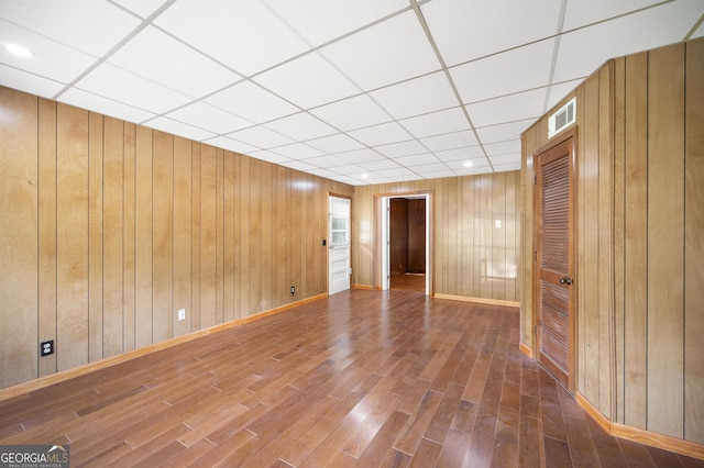 unfurnished room featuring a paneled ceiling, hardwood / wood-style floors, and wood walls