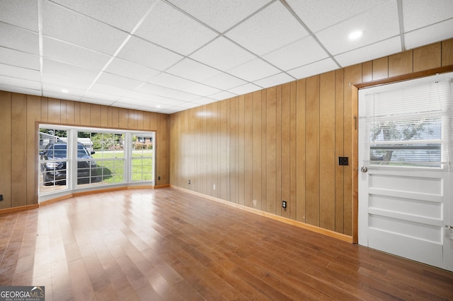 unfurnished living room featuring wooden walls, hardwood / wood-style floors, and a drop ceiling