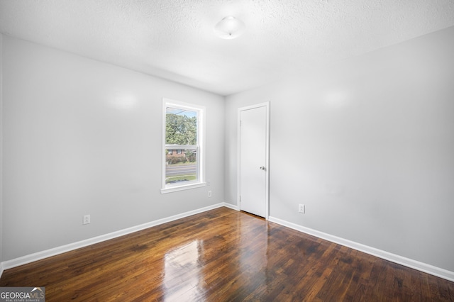 spare room featuring a textured ceiling and dark hardwood / wood-style flooring