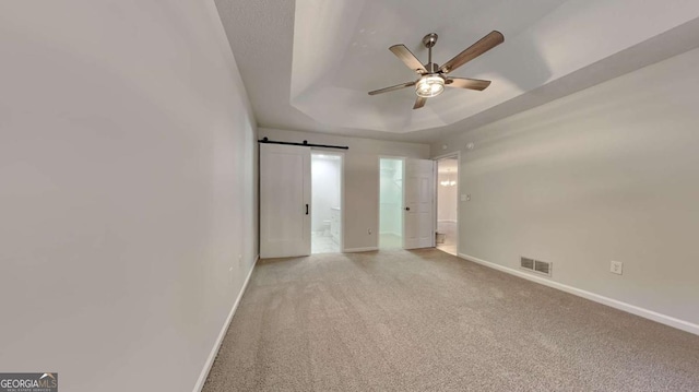 unfurnished bedroom featuring a barn door, ceiling fan, a tray ceiling, and light carpet