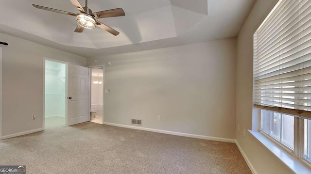 spare room featuring a tray ceiling, light colored carpet, and ceiling fan