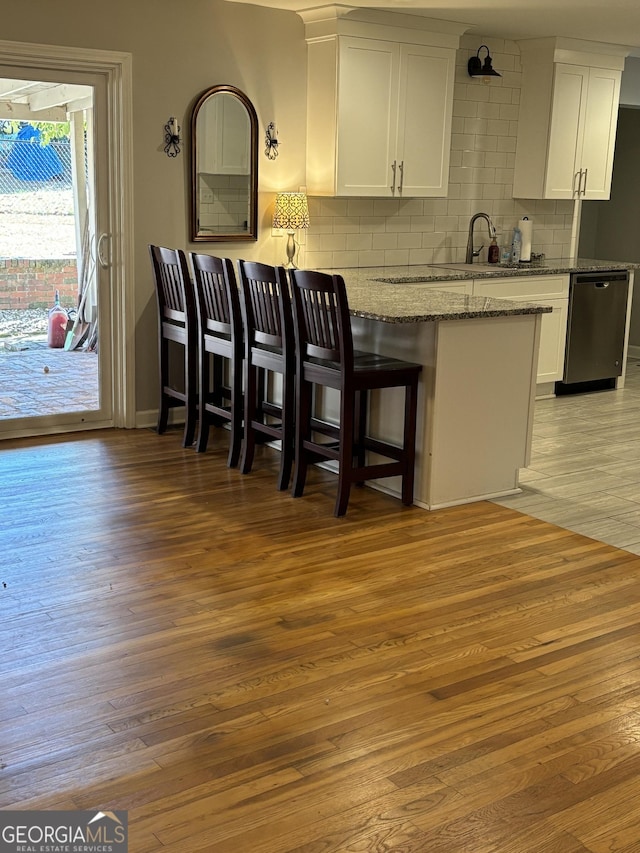 kitchen featuring white cabinets, light wood-style flooring, a peninsula, light stone countertops, and stainless steel dishwasher