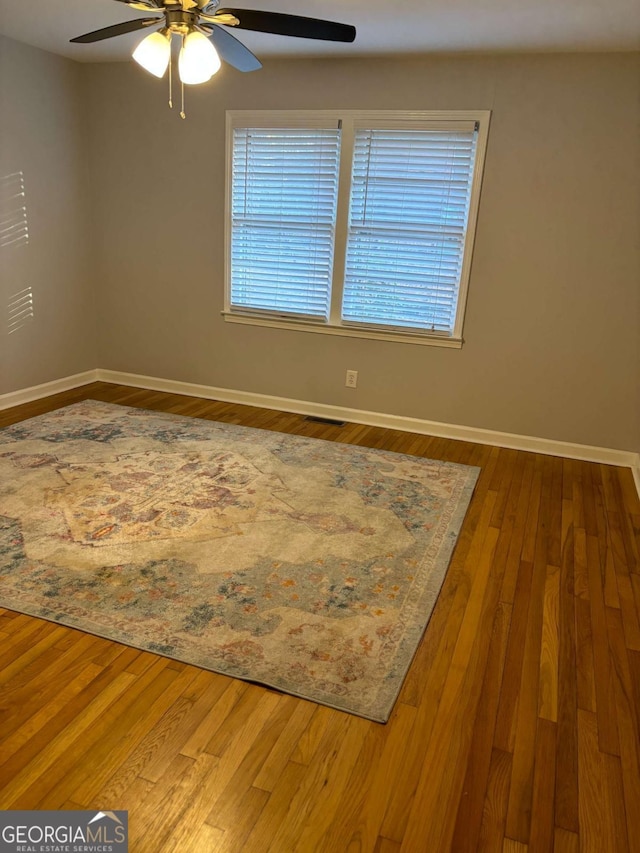 unfurnished room featuring ceiling fan, plenty of natural light, wood finished floors, and baseboards