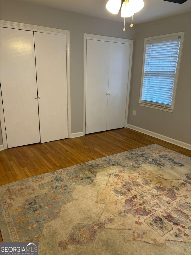 unfurnished bedroom featuring wood finished floors, two closets, and baseboards