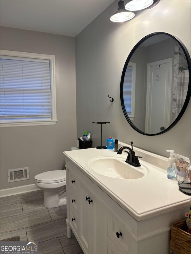 bathroom featuring toilet, vanity, visible vents, and baseboards