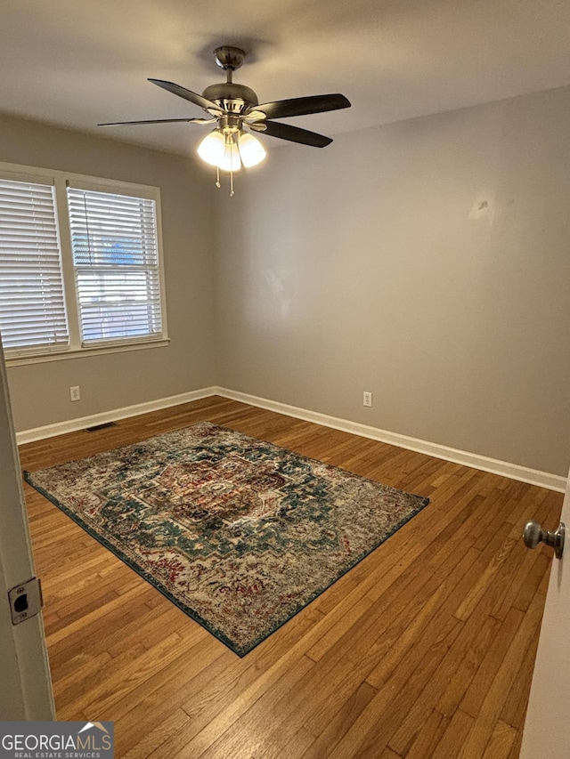 empty room with dark wood-style floors, a ceiling fan, visible vents, and baseboards