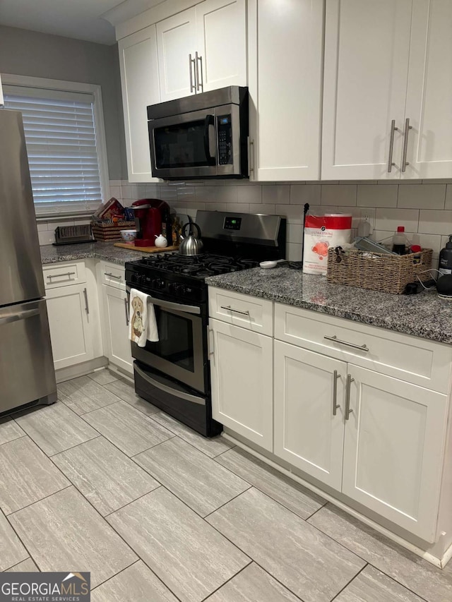 kitchen featuring white cabinets, dark stone counters, stainless steel appliances, and backsplash