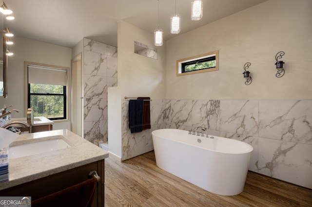 bathroom with a washtub, vanity, hardwood / wood-style flooring, and tile walls