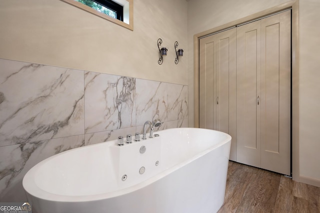 bathroom with hardwood / wood-style flooring, a bathing tub, and tile walls