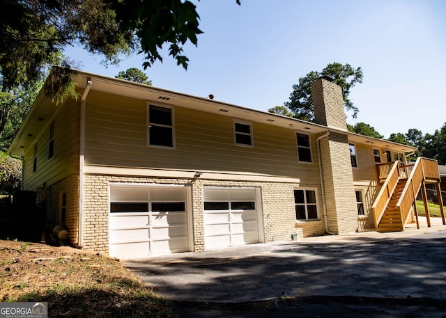 view of front facade featuring driveway, a chimney, stairs, a garage, and brick siding