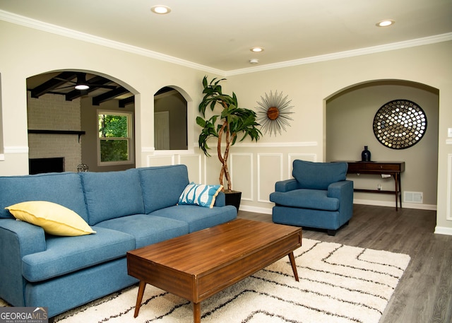 living room with visible vents, a brick fireplace, crown molding, and wood finished floors