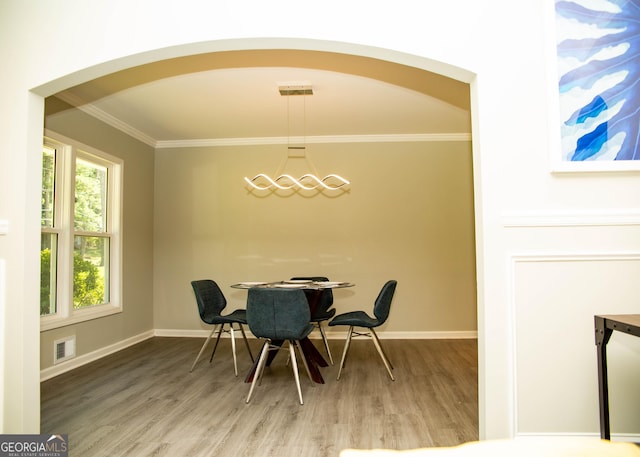 dining room with wood finished floors, arched walkways, and ornamental molding