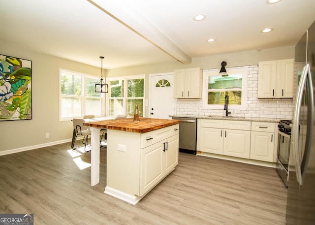 kitchen featuring light wood-type flooring, wood counters, tasteful backsplash, appliances with stainless steel finishes, and white cabinets