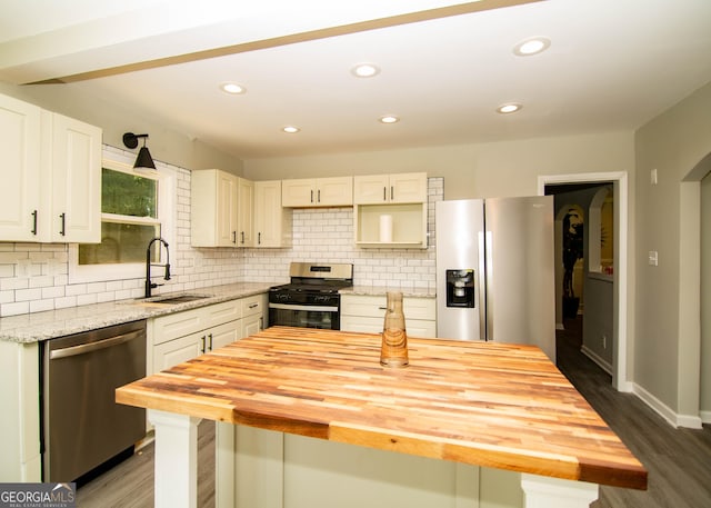 kitchen with dark wood-style floors, a sink, decorative backsplash, appliances with stainless steel finishes, and wood counters