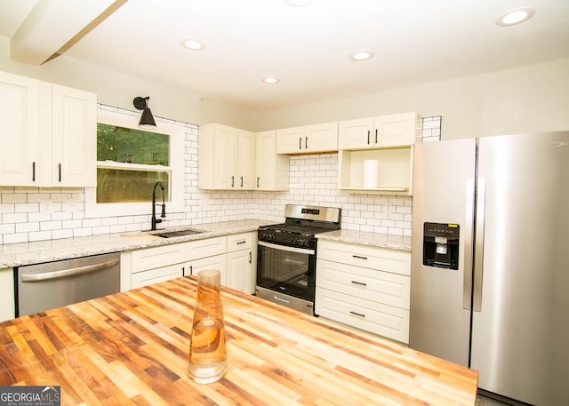 kitchen featuring tasteful backsplash, wooden counters, appliances with stainless steel finishes, white cabinetry, and a sink