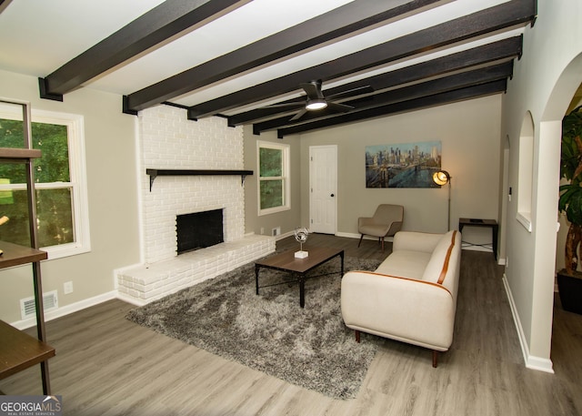 living area with a ceiling fan, wood finished floors, visible vents, beam ceiling, and a fireplace