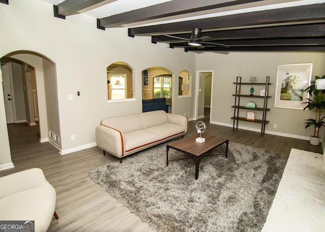 living room with wood finished floors, baseboards, arched walkways, ceiling fan, and beamed ceiling