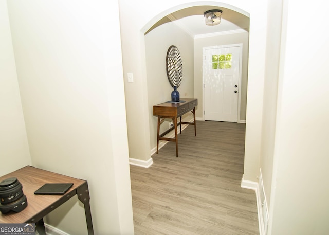 hall featuring arched walkways, light wood finished floors, crown molding, and baseboards