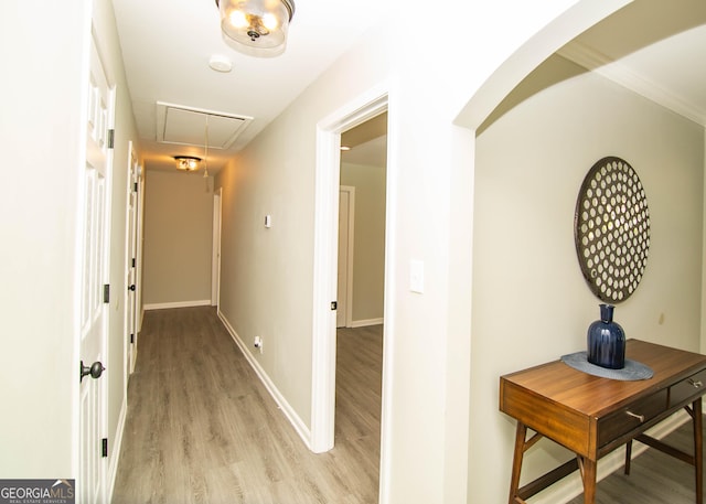 hallway featuring arched walkways, attic access, light wood-type flooring, and baseboards