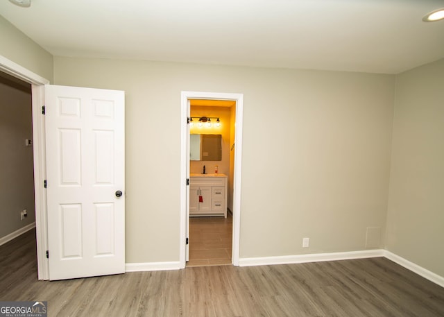 unfurnished bedroom with wood finished floors, baseboards, ensuite bathroom, and a sink