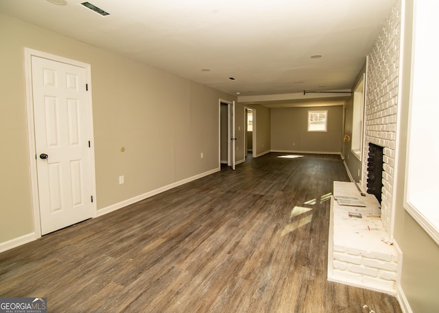 unfurnished living room with a brick fireplace, dark wood-style floors, and baseboards