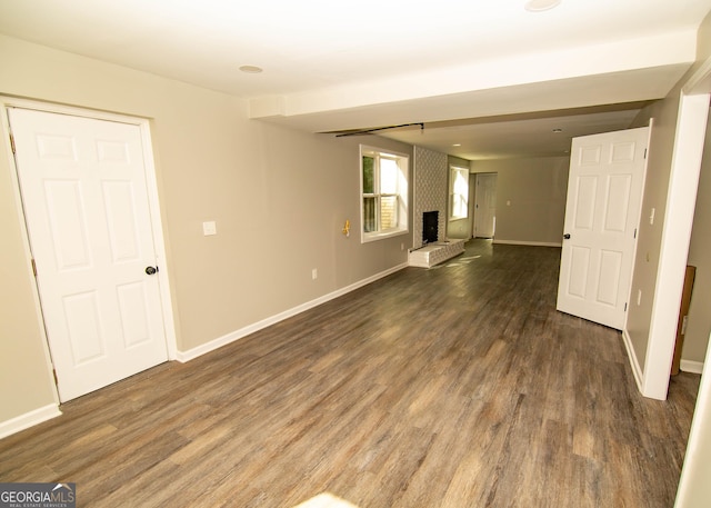 unfurnished living room featuring a brick fireplace, wood finished floors, and baseboards