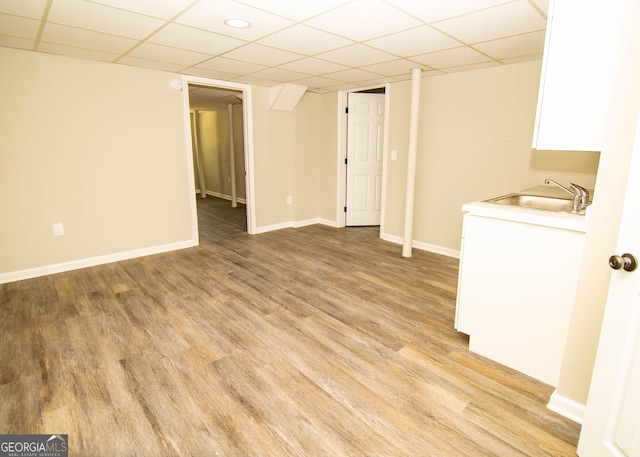 interior space with a sink, a drop ceiling, baseboards, and light wood-style flooring