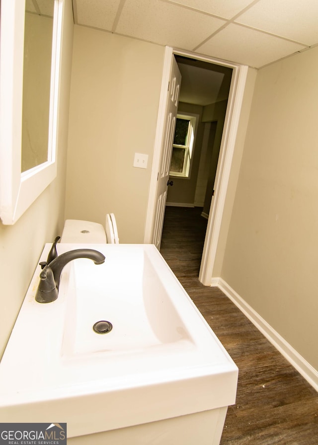 bathroom with baseboards, a paneled ceiling, and wood finished floors