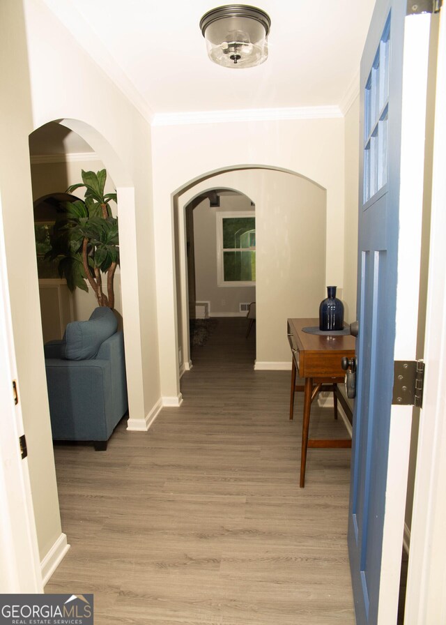 corridor featuring arched walkways, light wood-style floors, and crown molding