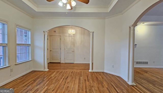 unfurnished room featuring crown molding, a tray ceiling, decorative columns, and hardwood / wood-style flooring