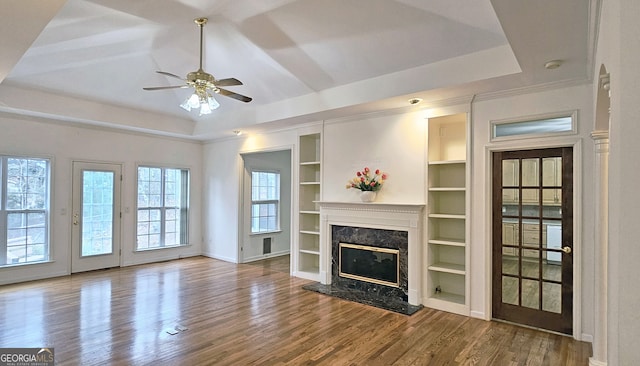 living room featuring a raised ceiling, a premium fireplace, hardwood / wood-style flooring, and built in features