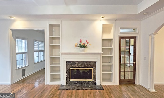 unfurnished living room featuring hardwood / wood-style floors, ornamental molding, built in features, and a premium fireplace