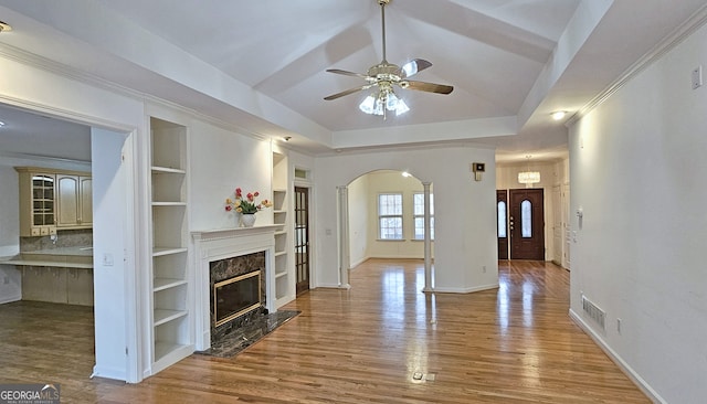 living room with wood-type flooring, a raised ceiling, built in features, ceiling fan, and a premium fireplace