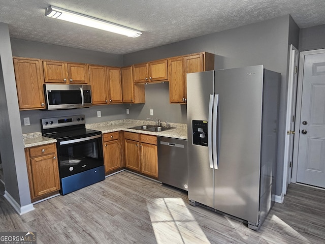 kitchen with sink, light wood-type flooring, a textured ceiling, and appliances with stainless steel finishes