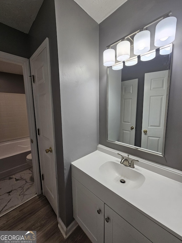 bathroom featuring vanity, a tub to relax in, a textured ceiling, and toilet