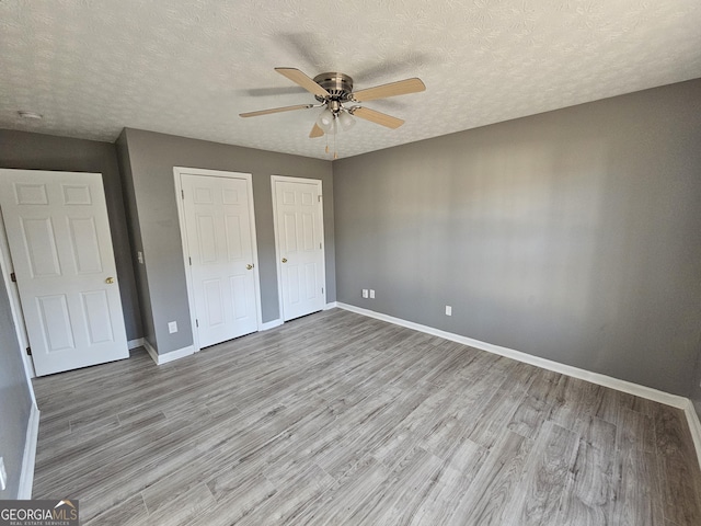 unfurnished bedroom with light hardwood / wood-style floors, a textured ceiling, and two closets